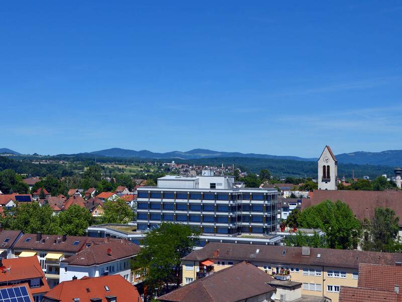 Blick über die Stadt: Im Fokus steht das Rathaus, zu sehen sind auch die Christuskirche und der Wasserturm, im Hintergrund erkennt man den Dinkelberg und Hotzenwald.