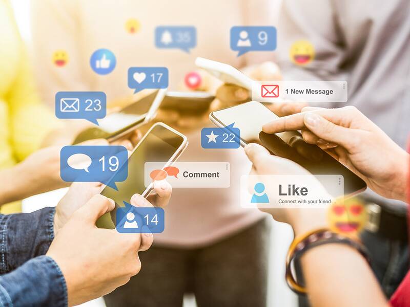 Mehrere junge Menschen stehen im Kreis und schicken sich mit  Smartphones Nachrichten, Kommetare, Likes und Bilder zu.