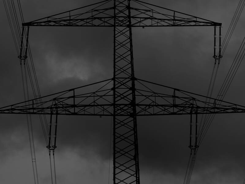 Teil eines Strommasten mit Hochspannungsleitungen vor dunklem, fast schwarzem Himmel 