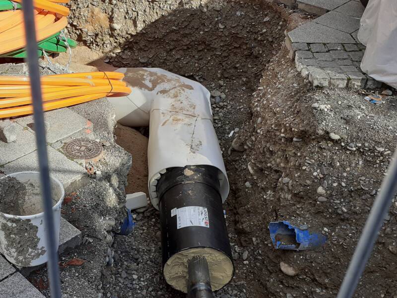 Blick in eine Baustelle: Man sieht eine Leitung, die mit Dämmmaterial ummantelt ist. Oben am Bildrand liegen bunte Kabel. 