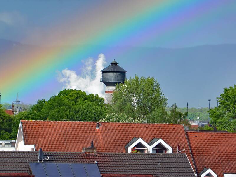 Bunter Regenbogen über der Stadt. Im Mittelpunkt des Bildes steht der Wasserturm, der noch leicht von dem darüber verlaufenden Regenbogen "berührt" wird.