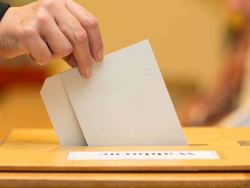 Ein Wahlzettel wird in eine Wahlurne geworfen. 