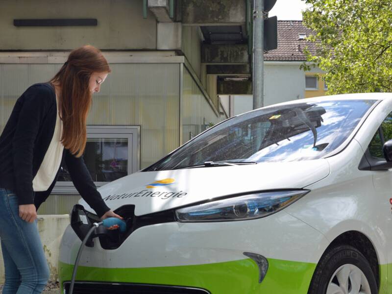 Eine junge Frau betankt en E-Car an einer  E-Station.