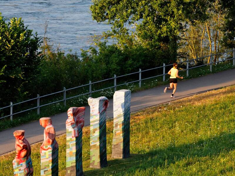 Der Adelberg mit Spazierweg, einem Jogger, Skulptur und Rhein