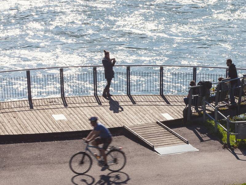Auf der Adelberg-Plattform am Rhein sitzen und stehen mehrere Personen, im Vordergrund ein Radfahrer.