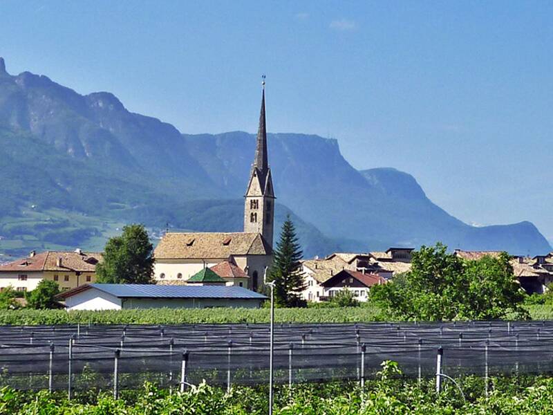 Blick aus der Ferne auf die Gemeinde Neumarkt. Prägnant im Zentrum ist der Kirchturm. Im Hintergrund sind Berge zu sehen. 