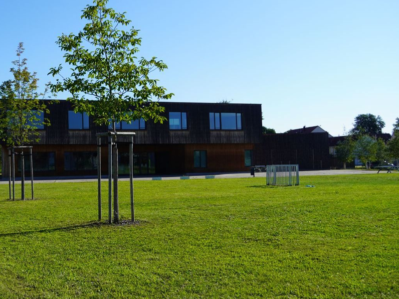 Blick von der Straße auf das bestehende Campus-Gebäude in Holzbauoptik. 
