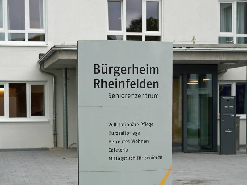 Blick auf den Eingang des Bürgerheims. Im Vordergrund steht eine Stele, auf der Bürgerheim Rheinfelden steht.