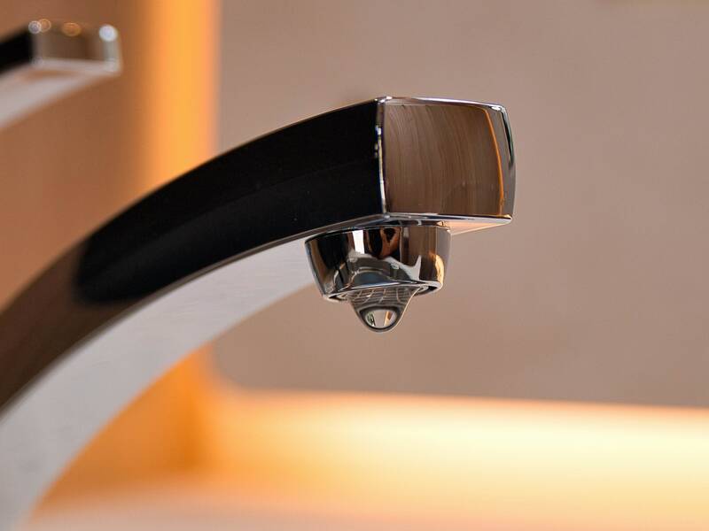 Silberner Wasserhahn, an dem ein halber Tropfen hängt.