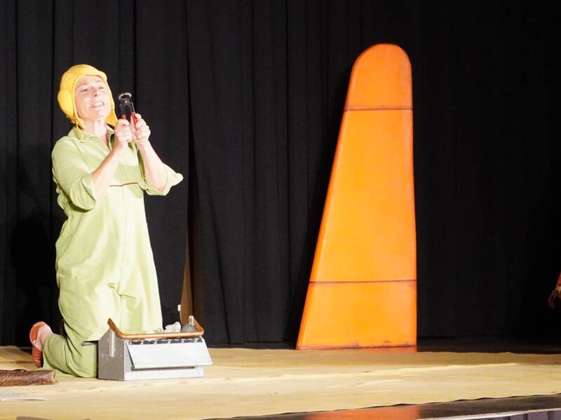 Kindertheatertage: Der kleine Prinz aus dem gleichnamigen Stück kniet auf der Bühne, eine Zange in der Hand. Am rechten Bildrand sieht man Teile eines abgestürzten Flugzeuges und den Piloten, der dieses zu reparieren versucht.  