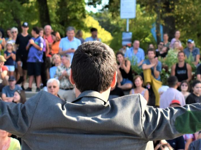 Ein Künstler mit dem Rücken zur Kamera wird vom Publikum im Hintergrund gefeiert. 
