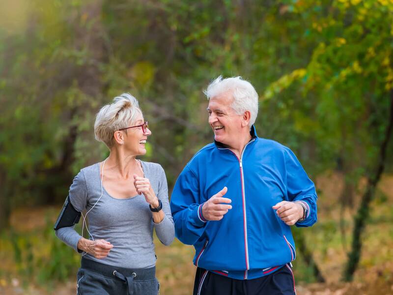 Zwei Senioren joggen durch einen Park.