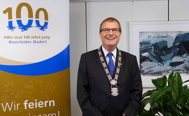 Oberbürgermeister Klaus Eberhardt mit Amtskette vor einem Banner zum 100-jährigen Stadtjubiläum.