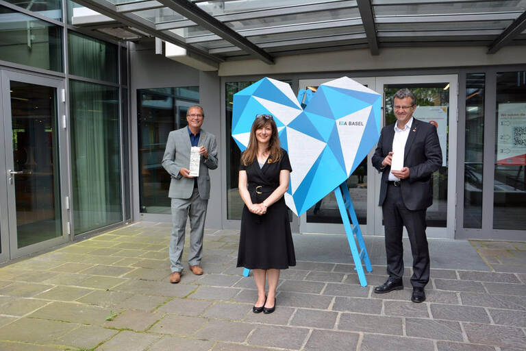 Drei Personen, Oberbürgermeister Klaus Eberhardt, Monica Linder-Guarnaccia und Stadtammann Franco Mazzi, stehen vor dem Eingang ins Rathaus um ein großes, in verschiedenen Blautönen gehaltenes Herz. 