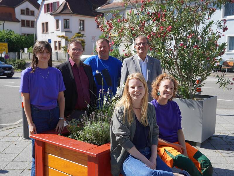 Das Initiatoren-Team der Klima-Kisten mit Oberbürgermeister Klaus Eberhardt rund um eine der stellenweise rot lackierten Kisten, die mit verschiedenen Pflanzen beflanzt sind. 