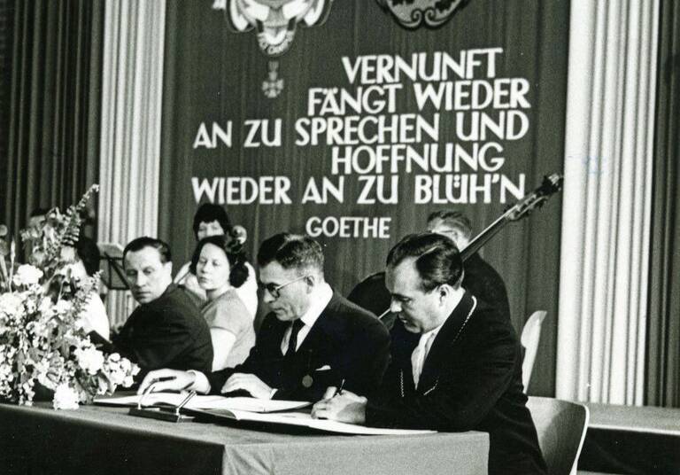 Historische Aufnahme: Unterzeichnung des Vertrags von Bürgermeister Maurice Sadorge und Bürgermeister Herbert King vor einem Banner mit einem Goethezitat. 