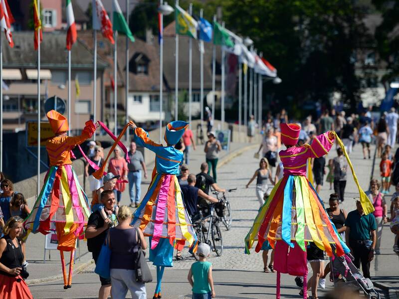 Ein Walk-Akt von drei Küsntlern in bunten Kostümen auf der Rheinbrücke