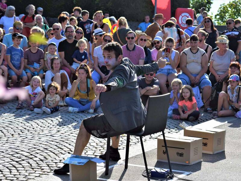 Ein Clown auf einem Stuhl, im Hintergrund lachende Zuschauer