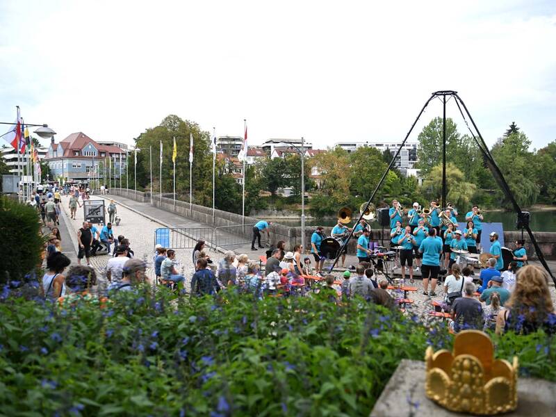 Brückensensationen 2026: Eine Blaskapelle in blauen T-Shirts spielt vor einem Publikum auf einer Brücke mit mehreren Fahnen im Hintergrund, während Menschen umhergehen.