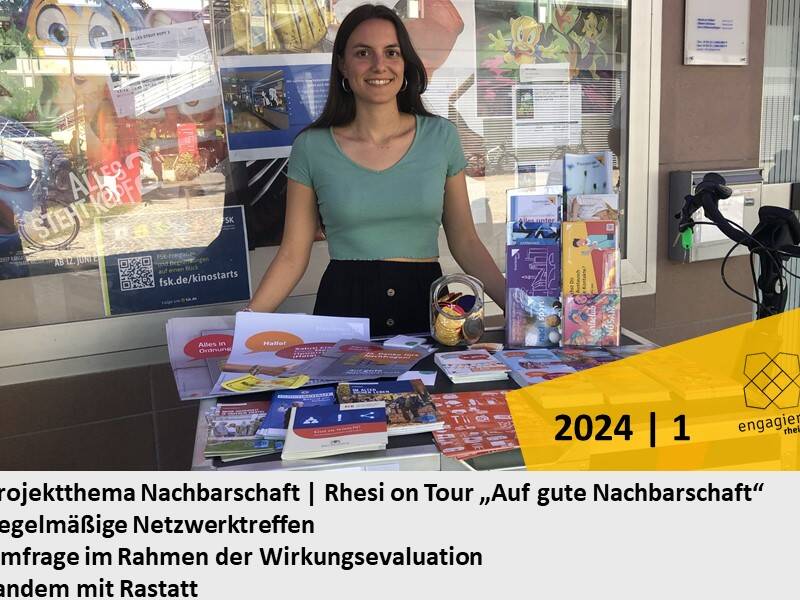 Eine Frau steht an einem Tisch mit Informationsmaterialien und lächelt, während im Hintergrund Plakate und eine Fahrradhalterung zu sehen sind.