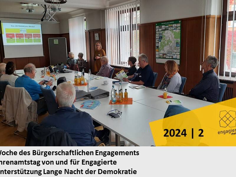 Eine Gruppe von Menschen sitzt an einem Konferenztisch und hört einer Präsentation zu, während an der Wand eine Projektion des ZEITBANKplus Modells zu sehen ist.