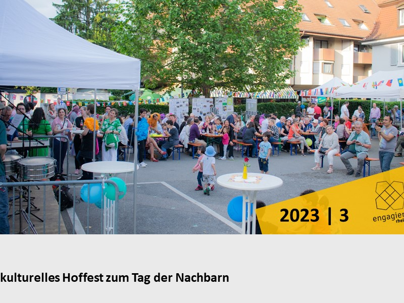 Eine große Gruppe von Menschen feiert bei einem interkulturellen Fest im Freien, mit Dekorationen und Sitzgelegenheiten unter Pavillons.