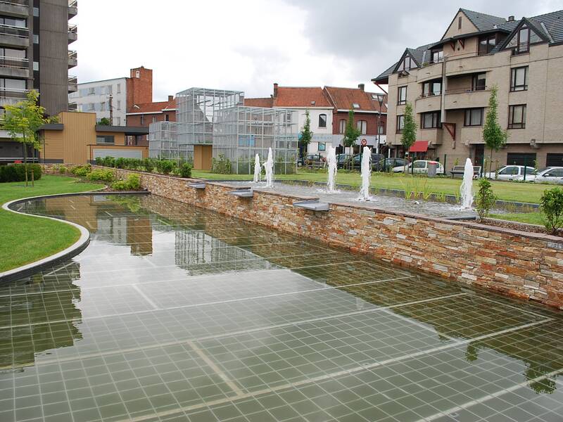 Ein moderner Stadtpark mit einem flachen Wasserbecken, kleinen Springbrunnen und umgeben von Wohngebäuden.