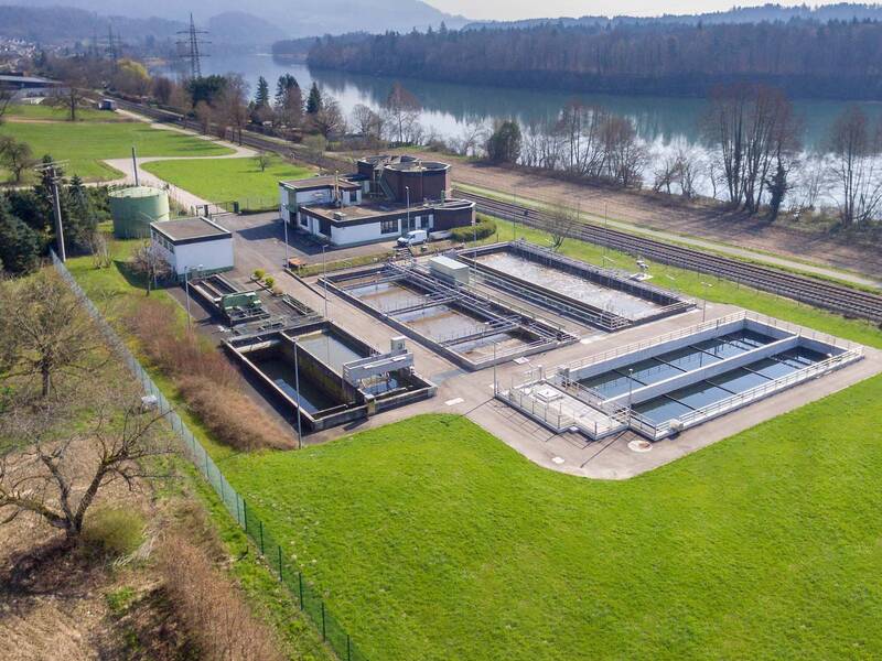 Eine Kläranlage befindet sich auf einem grünen Gelände am Ufer eines Flusses, umgeben von Bäumen und Landschaft.