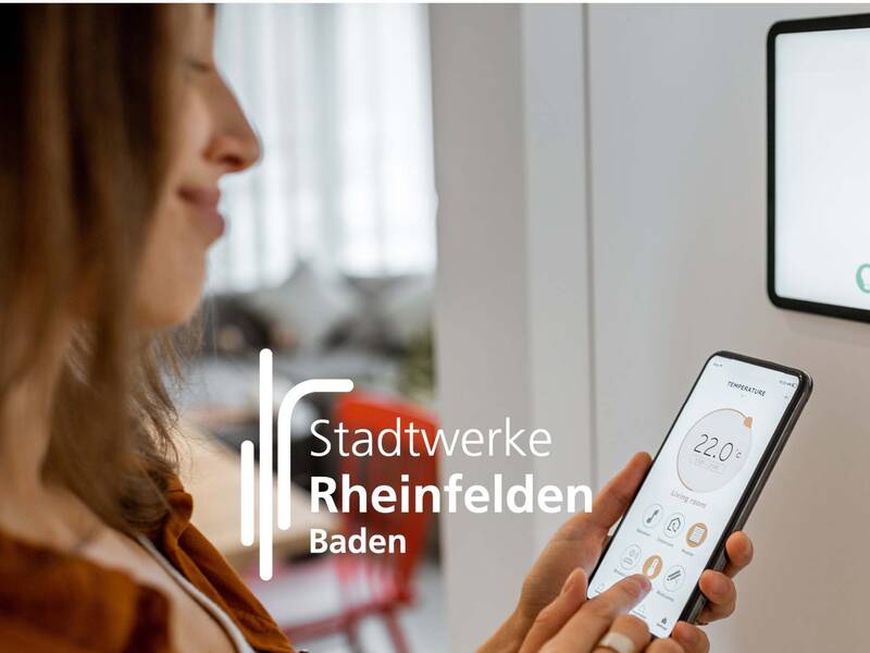 Eine Frau nutzt eine App auf ihrem Smartphone, um die Temperatur in einem Raum zu steuern, während im Vordergrund das Logo der Stadtwerke Rheinfelden Baden zu sehen ist.