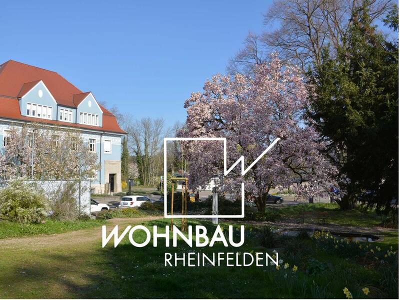 Ein blaues Haus mit rotem Dach steht neben blühenden Bäumen und einem grünen Garten unter einem wolkenlosen Himmel.