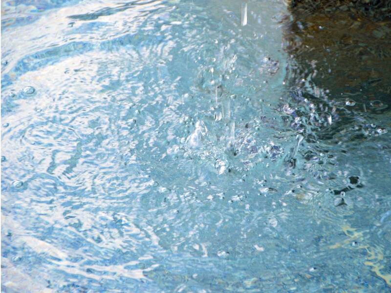 Wasseroberfläche mit fallenden Regentropfen, die Wellen und Spritzer erzeugen.