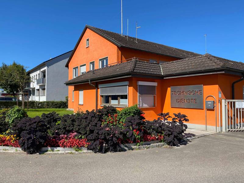 Orange gestichenes zweistöckiges Gebäude, in dem die Technischen Dienste untergebracht sind. Davor ein Blumenbeet.