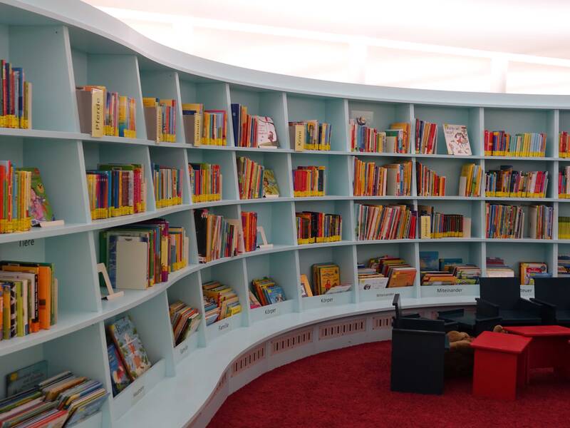 Stadtbibliothek: Kinder-Insel mit vielen Büchern in blauen, geschwungenen Regalen.