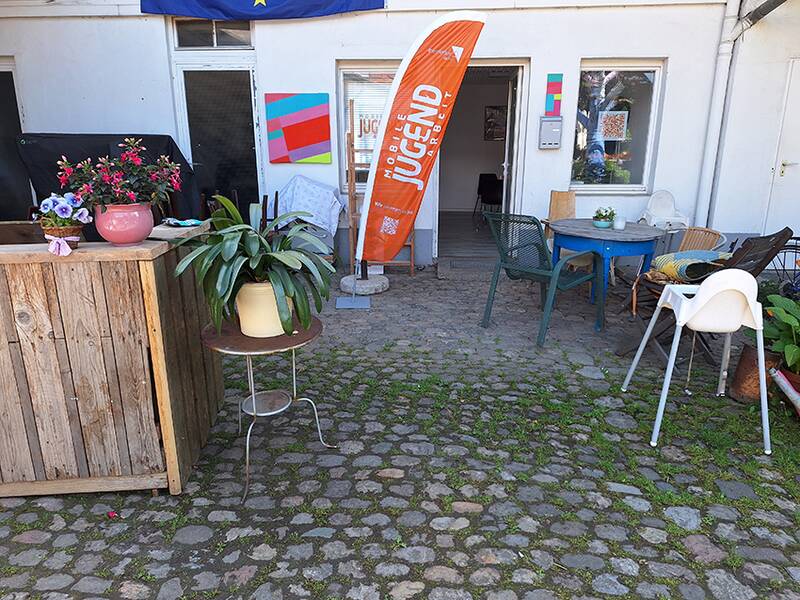Büro der Mobilen Jugendarbeit, vor dem verstreut unterschiedliche Tische und Stühle stehen.