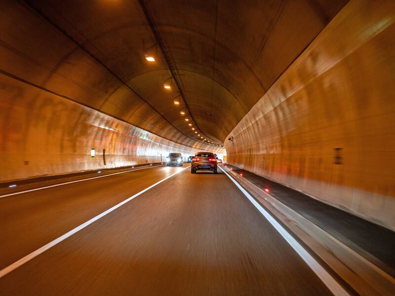 Innen in einem Straßentunnel mit Rücklichtern eines vorausfahrenden Fahrzeugs.