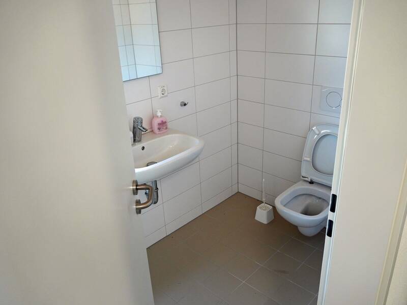 Ein kleines Badezimmer mit einem Waschbecken und einer Toilette, beide an einer gefliesten Wand, und einer Flasche Seife auf dem Waschbecken.