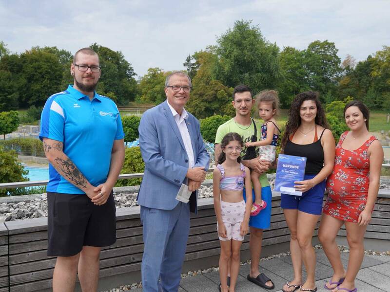 Gruppenbild: Bäderbetriebsleiter Tobias Wiener und OB Klaus Eberhardt freuen sich über den 75.000 Badegast. Über die kleine Aufmerksamkeit freut sich eine Familie aus Schwörstadt.