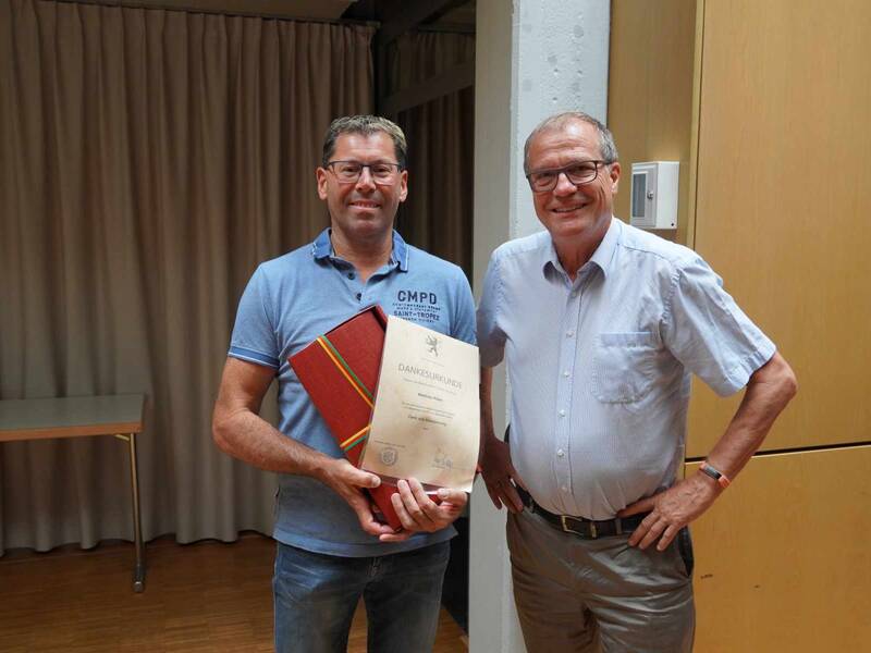 Oberbürgermeister Klaus Eberhardt gratuliert dem Leiter der Technischen Dienste, Matthias Huber, zu seinem 25-jährigen Jubiläum. Beide Personen blicken in die Kamera. Der Jubilar hält eine Urkunde und ein Geschenk in den Händen. 