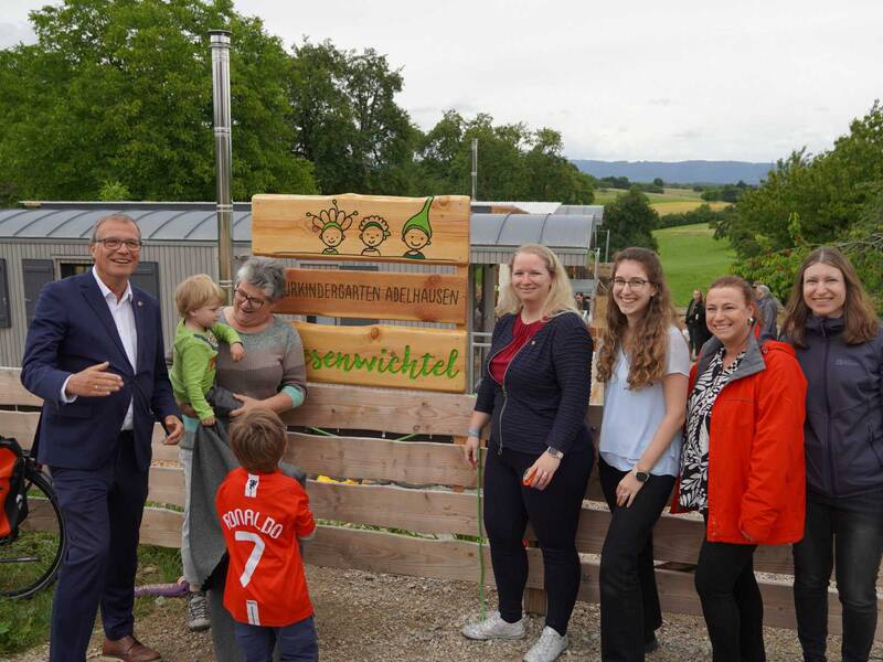 Naturkita Adelhausen: Oberbürgermeister Klaus Eberhardt enthüllt zusammen mit der Adelhausener Ortsvorsteherin Silvia Rütschle, Bürgermeisterin Kristin Fuchs  und der Leiterin des Amtes für Familie, Jugend und Senioren, Nicole Riße-Hasenkamp (rote Jacke) sowie deren Mitarbeiterinnen das Namensschild der Einrichtung. 