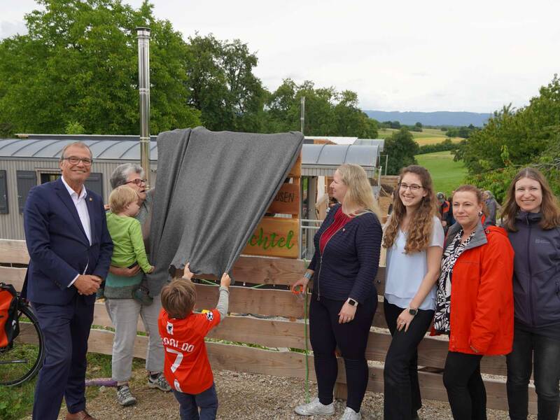 Naturkita Adelhausen: Oberbürgermeister Klaus Eberhardt enthüllt zusammen mit der Adelhausener Ortsvorsteherin Silvia Rütschle, Bürgermeisterin Kristin Fuchs  und der Leiterin des Amtes für Familie, Jugend und Senioren, Nicole Riße-Hasenkamp (rote Jacke) sowie deren Mitarbeiterinnen das Namensschild der Einrichtung. 