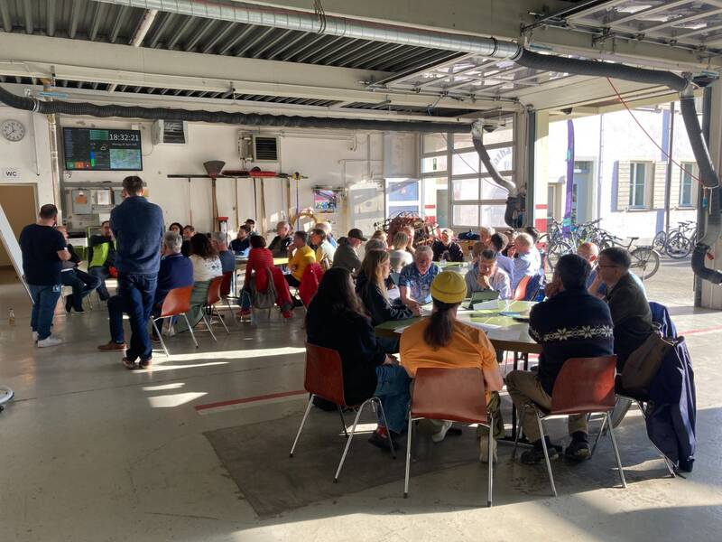 Infoabend E-Mobilität: Rund 50 Personen sitzen verteilt an Thementischen.