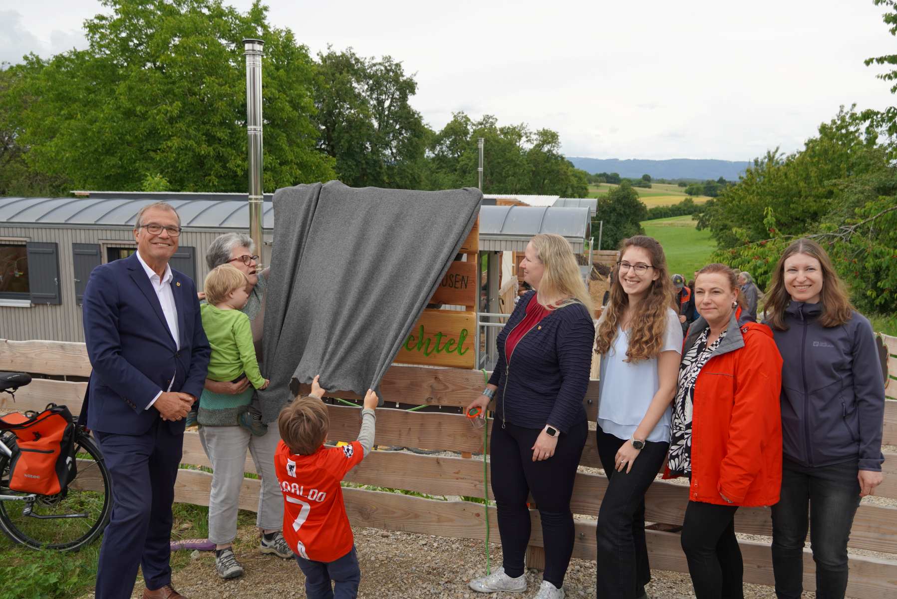 Naturkita Adelhausen: Oberbürgermeister Klaus Eberhardt enthüllt zusammen mit der Adelhausener Ortsvorsteherin Silvia Rütschle, Bürgermeisterin Kristin Fuchs  und der Leiterin des Amtes für Familie, Jugend und Senioren, Nicole Riße-Hasenkamp (rote Jacke) sowie deren Mitarbeiterinnen das Namensschild der Einrichtung. 
